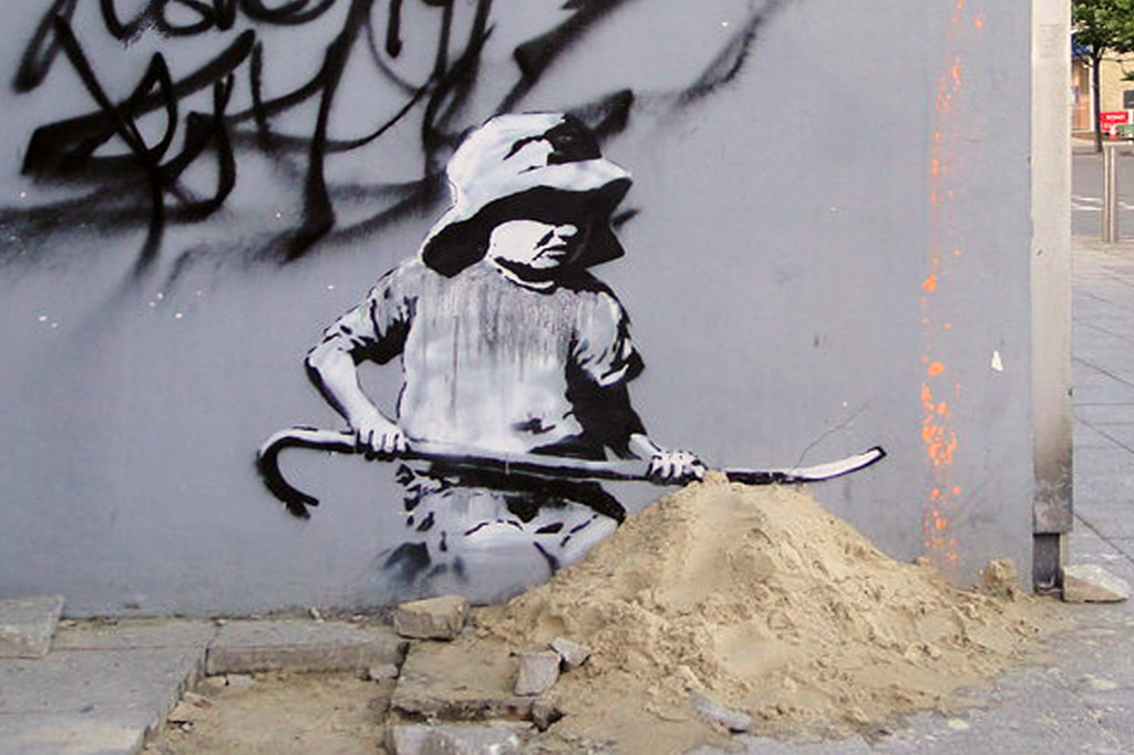 stensil of a child digging in the sand, the subject of a graffiti artwork bearing the hallmarks of street artist Banksy on a wall in Lowestoft on the East coast of England on August 8, 2021